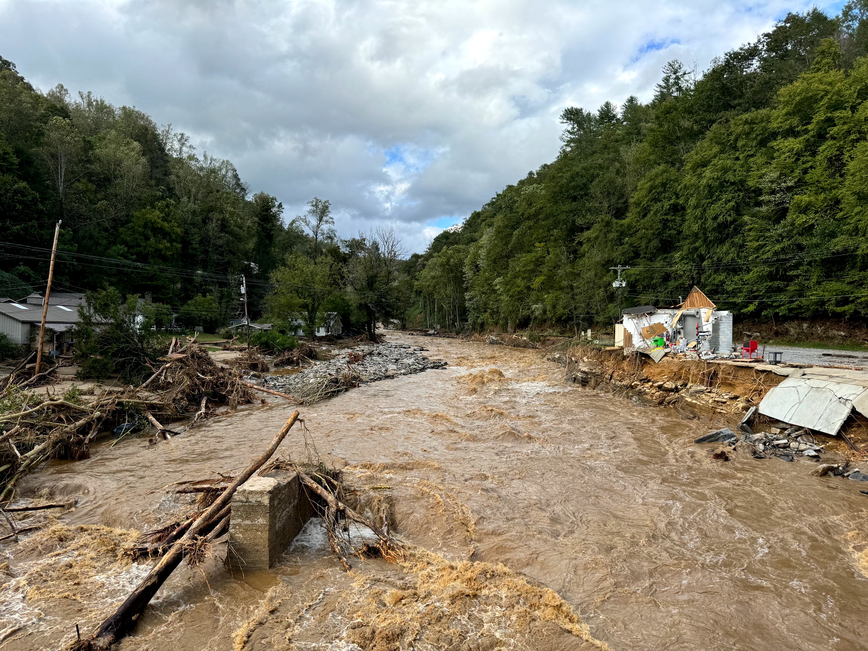 A destroyed road and structures with an overflowing brown river