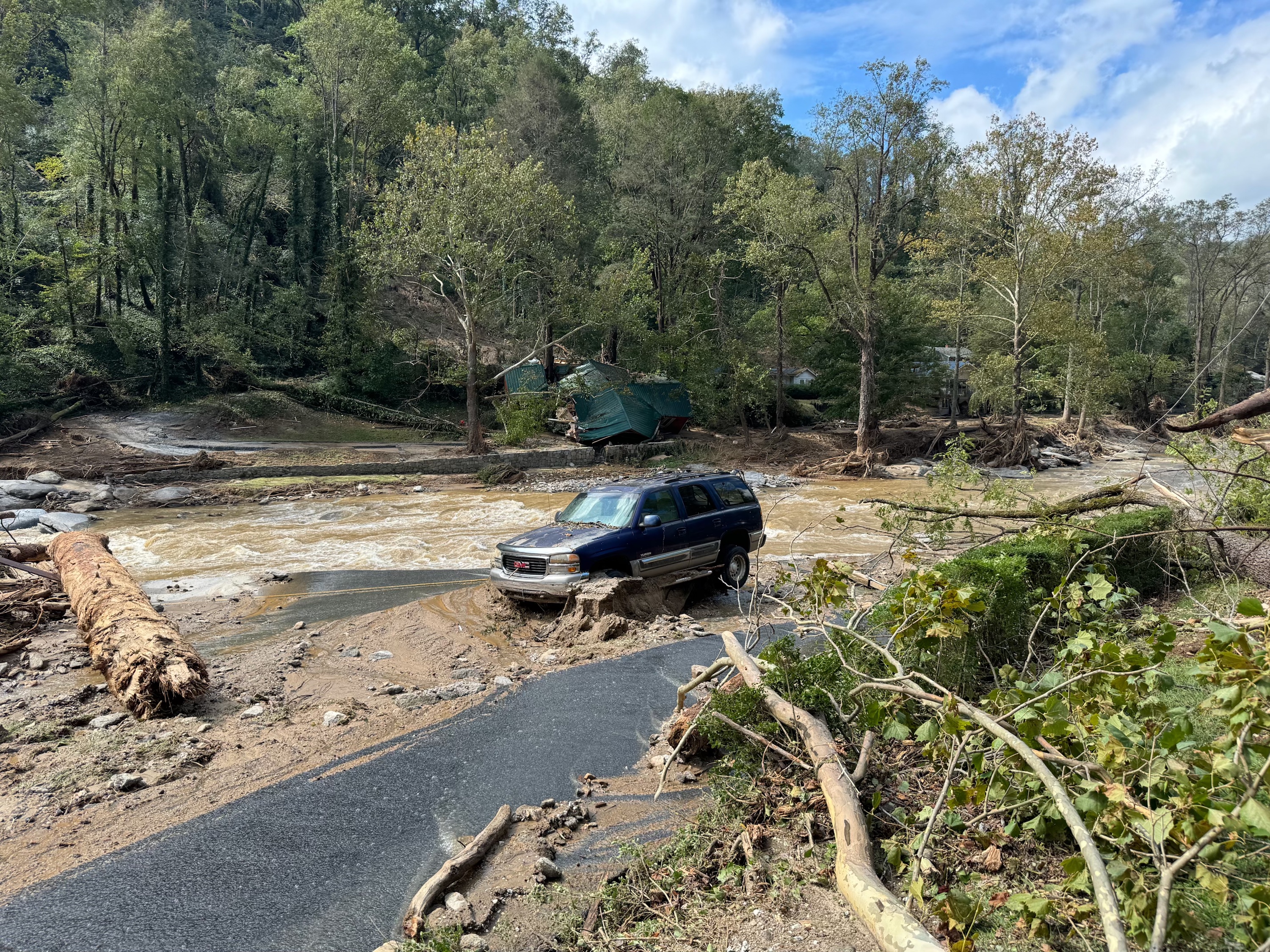 An abandoned car by a surging brown river