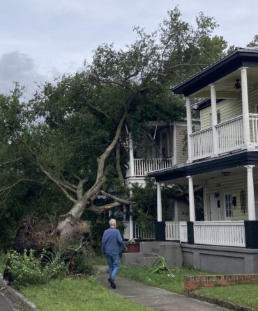 A fallen tree on a house. A man walks toward the house.