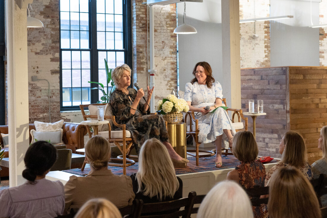 Two women talk, seated, in front of an audience