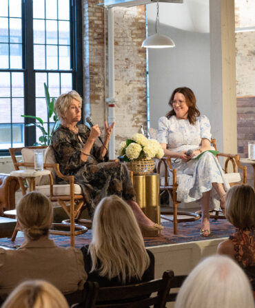 Two women talk, seated, in front of an audience