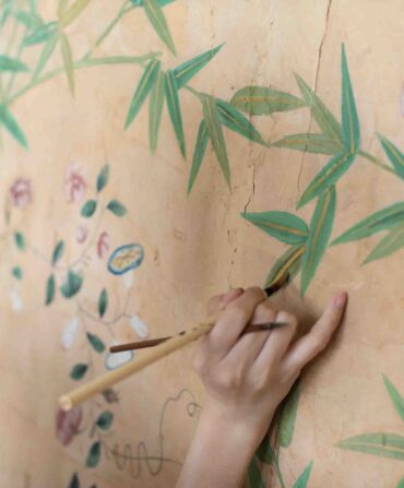 A woman paints leaves on a wall of wallpaper