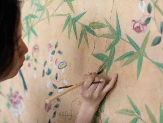 A woman paints leaves on a wall of wallpaper