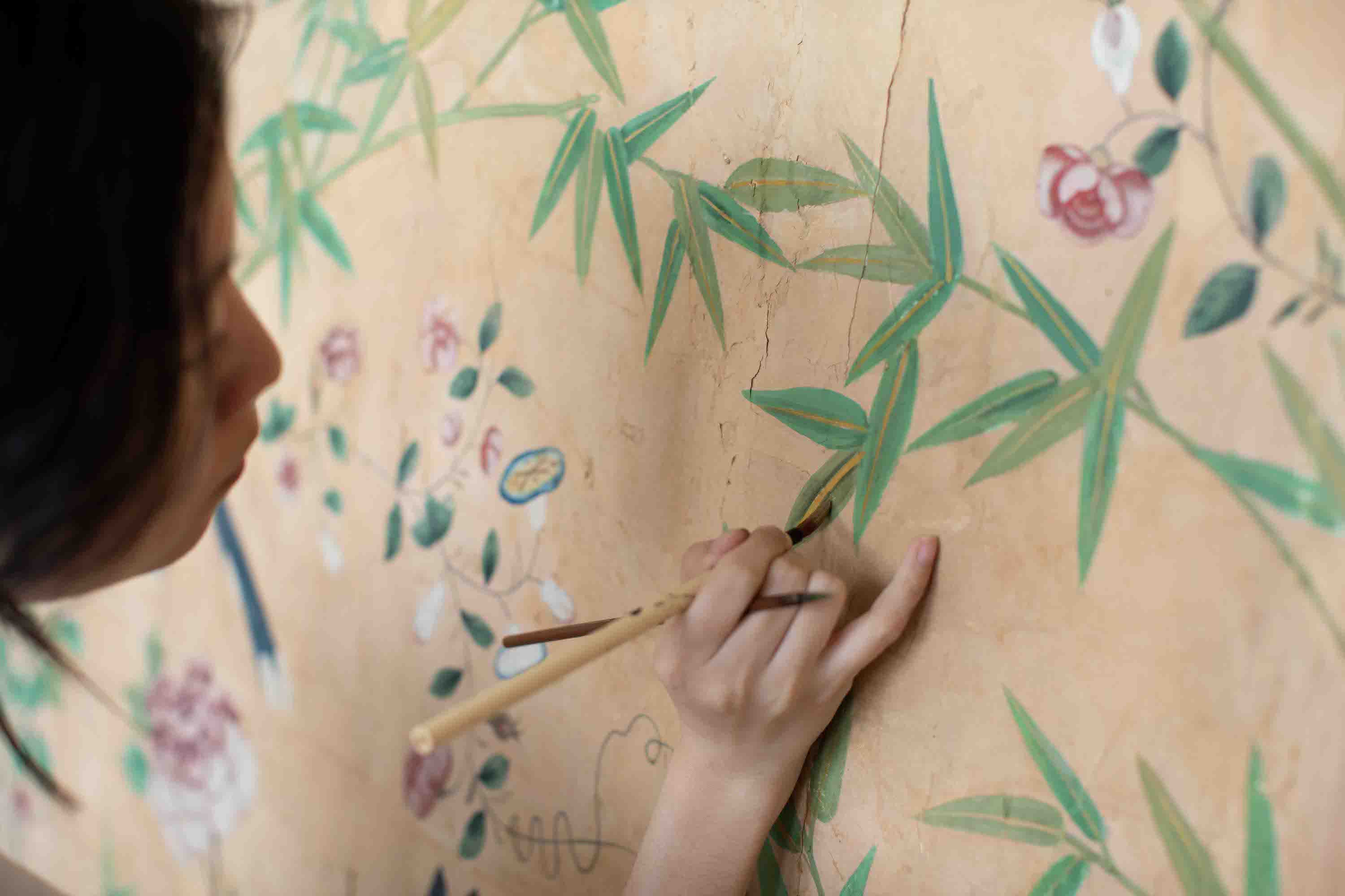 A woman paints leaves on a wall of wallpaper