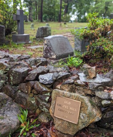 A plaque that reads "Old Chapel Hill Cemetery" with tombstones in the background.