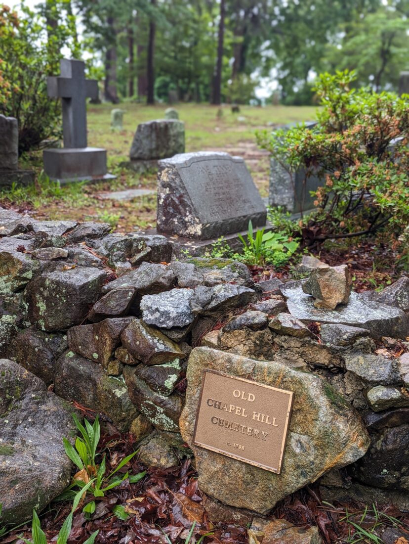 A plaque that reads "Old Chapel Hill Cemetery" with tombstones in the background.