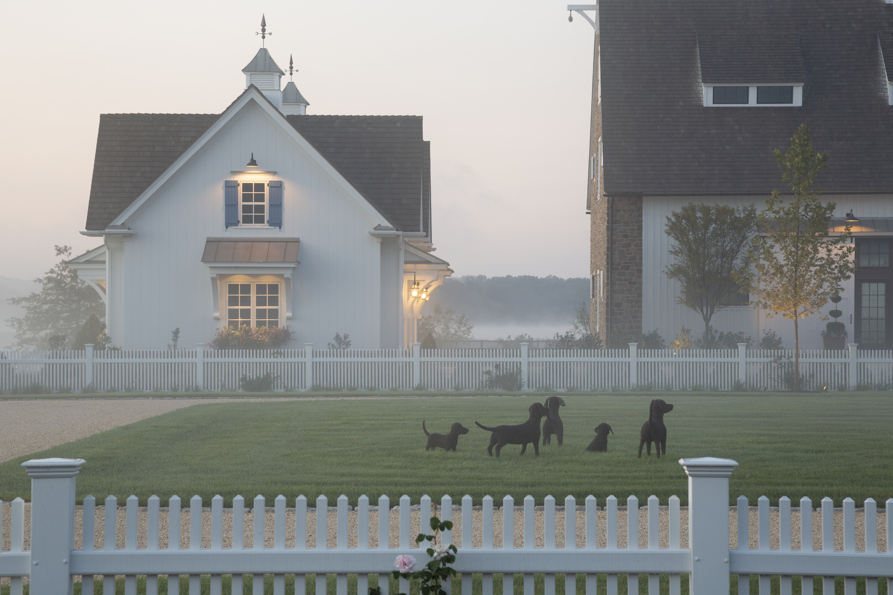 The yard before a carriage house. There is fog and stuffed moss dogs on the grass.