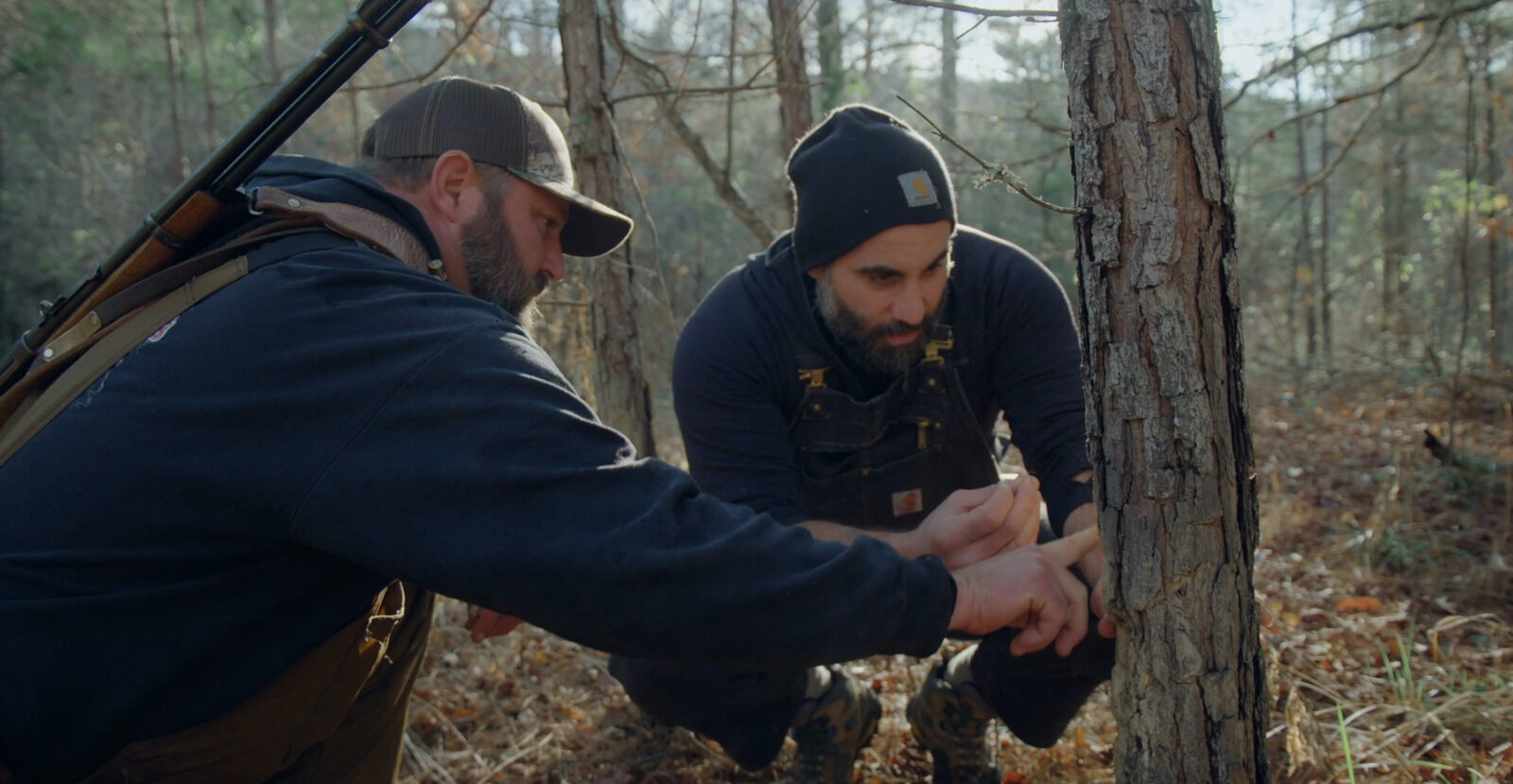 Two men crouch by a tree