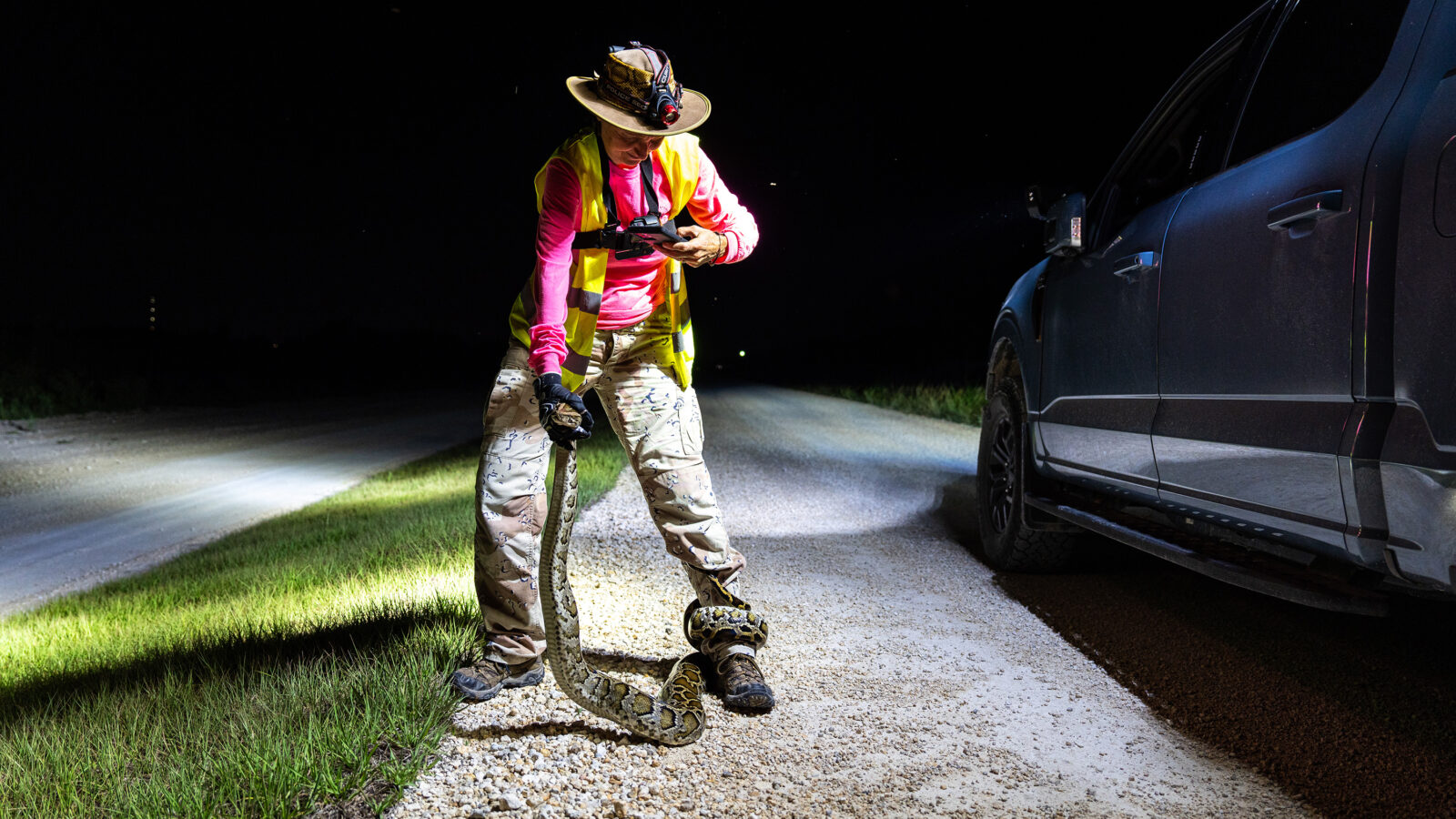 A woman taking a photo of a python wrapped around her leg