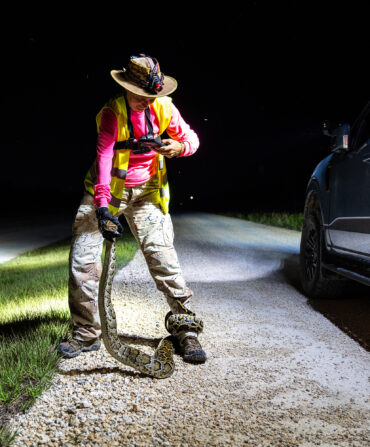 A woman taking a photo of a python wrapped around her leg