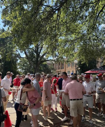 A large group of people dressed in red gather under trees