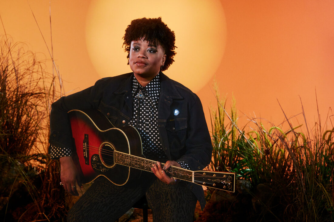 A portrait of a woman with a guitar against an orange background