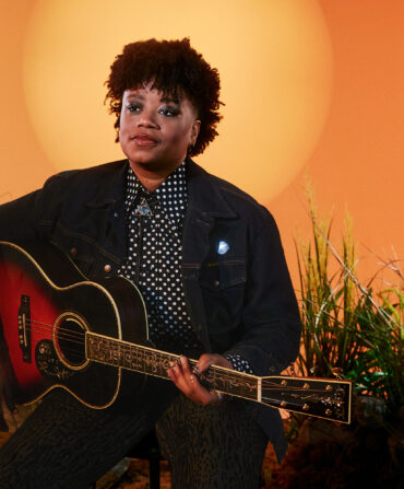 A portrait of a woman with a guitar against an orange background