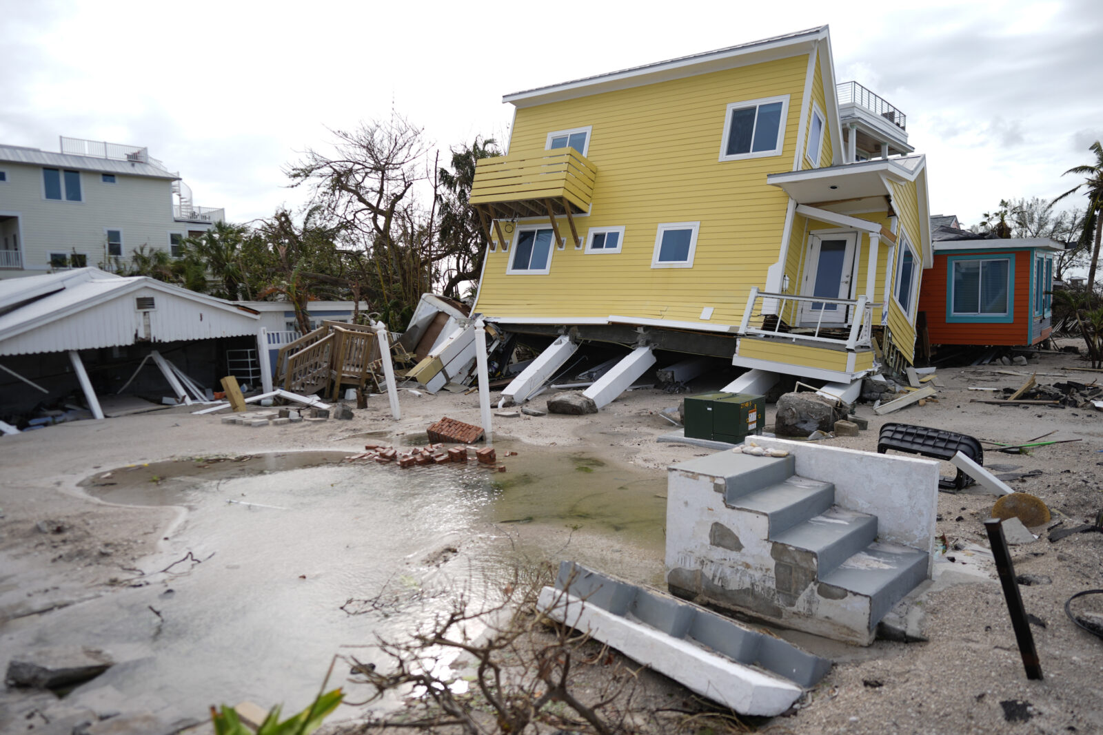 A house, center, lies toppled off its stilts after the passage of Hurricane Milton, alongside an empty lot where a home was swept away by Hurricane Helen, in Bradenton Beach on Anna Maria Island, Fla., Thursday, Oct. 10, 2024.