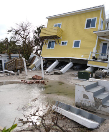 A house, center, lies toppled off its stilts after the passage of Hurricane Milton, alongside an empty lot where a home was swept away by Hurricane Helen, in Bradenton Beach on Anna Maria Island, Fla., Thursday, Oct. 10, 2024.