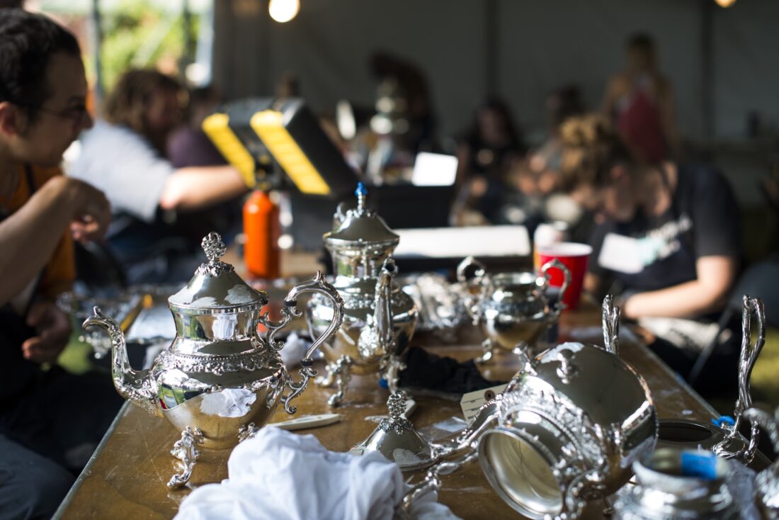 A spread of silver on a table with people cleaning it