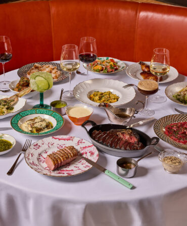 A spread of steak and meats on a white table clothed table in a red booth