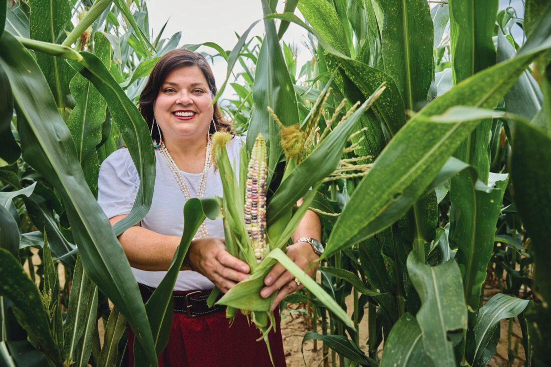 A woman holds a cob of colorful corn in a cornfield