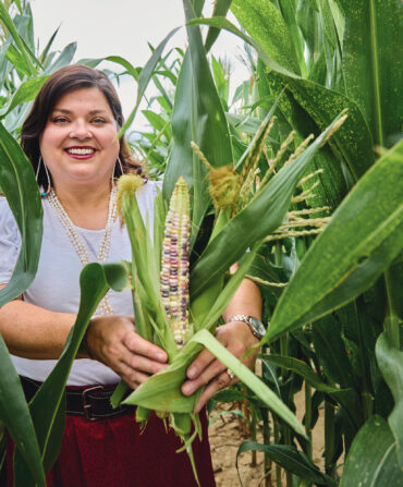 A woman holds a cob of colorful corn in a cornfield