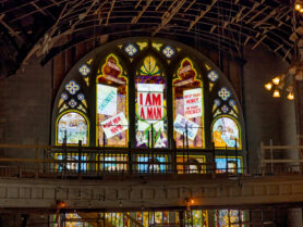 An arched stain glass window shows marching people