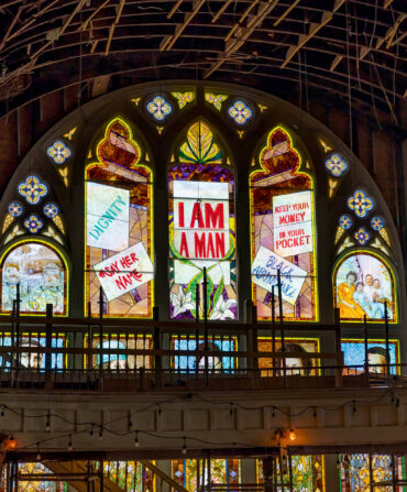 An arched stain glass window shows marching people