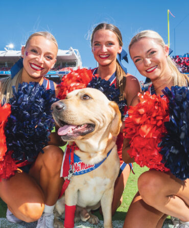 Cheerleaders smile and crowd around a yellow lab