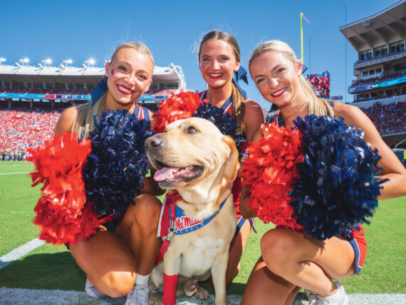 Cheerleaders smile and crowd around a yellow lab