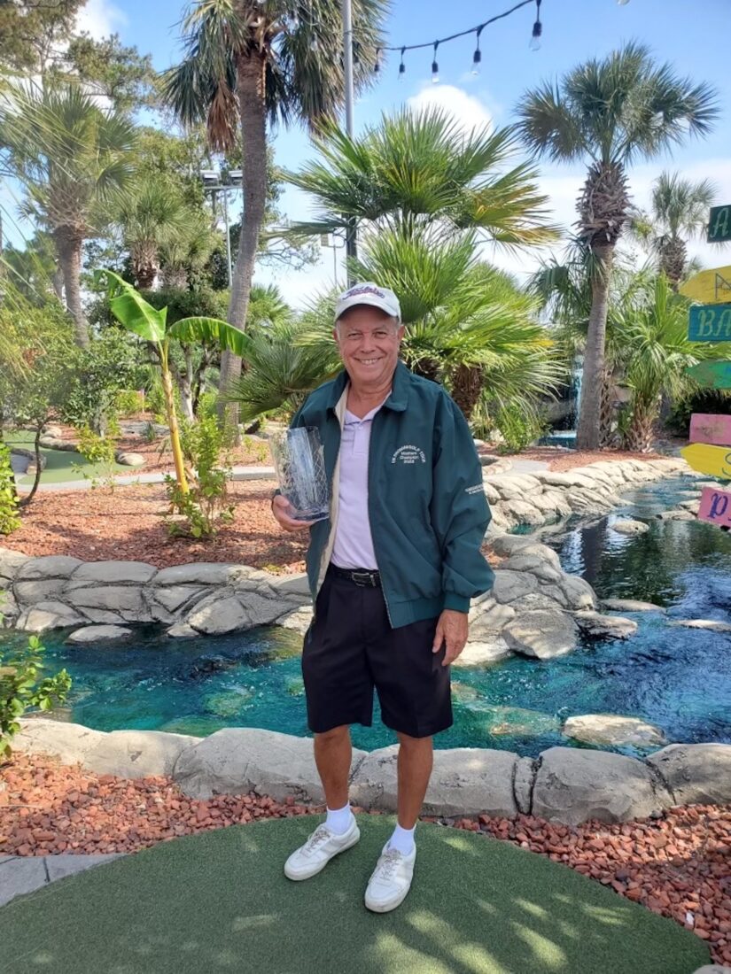 A man holds a glass trophy on a mini golf course