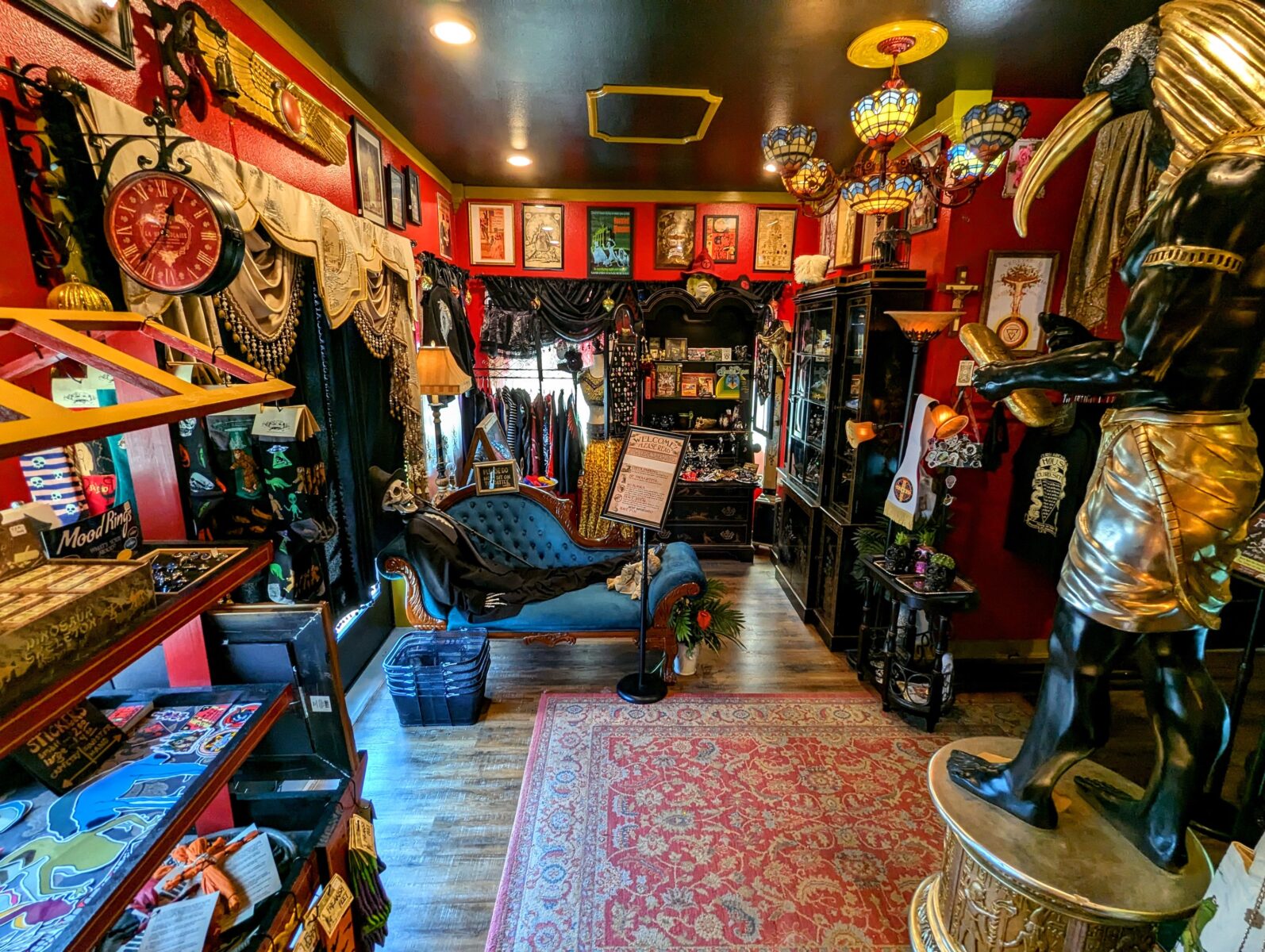 Inside a red-walled oddity shop with posters, black cabinets, and statues