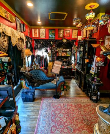 Inside a red-walled oddity shop with posters, black cabinets, and statues