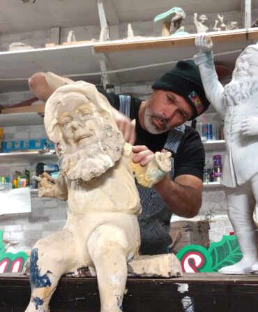 A man in a studio restores statues of gnomes