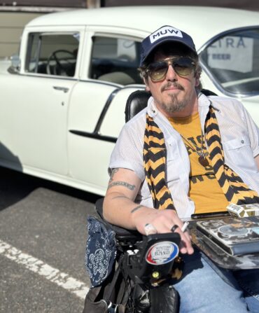 A portrait of a man with a black and yellow scarf in front of an old car