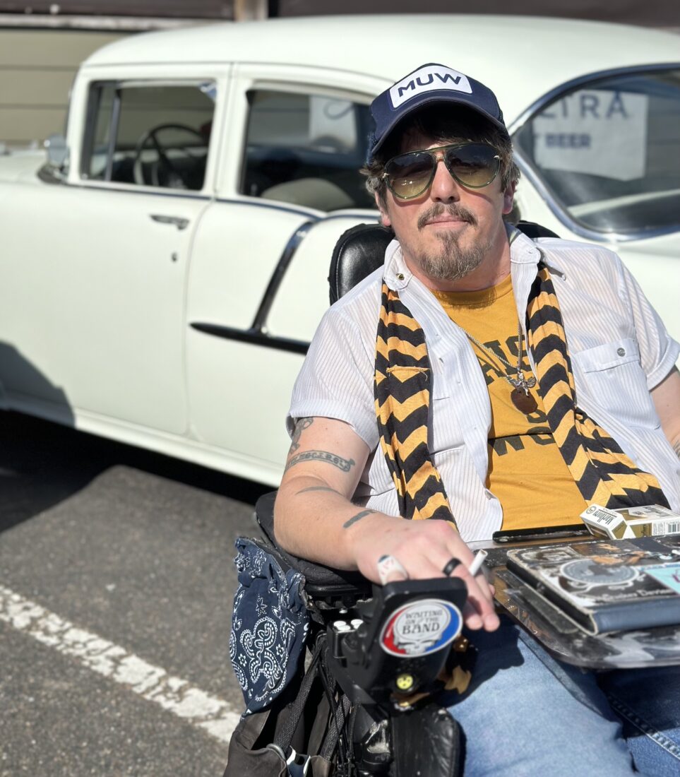 A portrait of a man with a black and yellow scarf in front of an old car