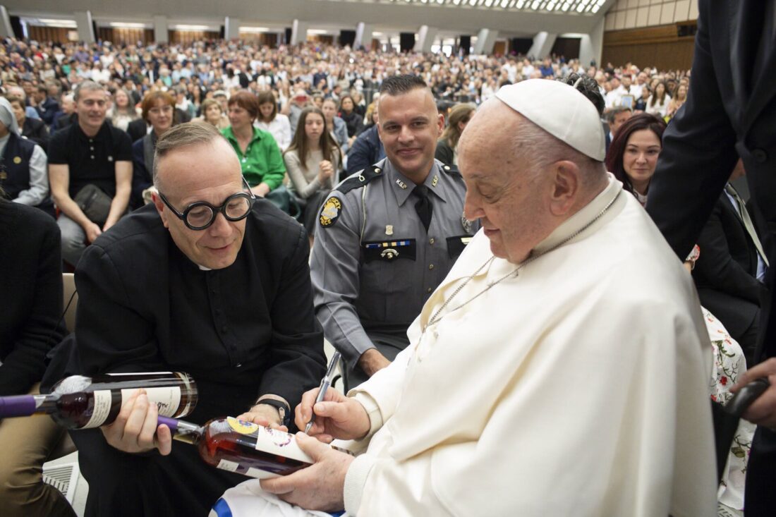 A priest and Pope Francis. Pope Francis holds bottles of bourbon and signs them