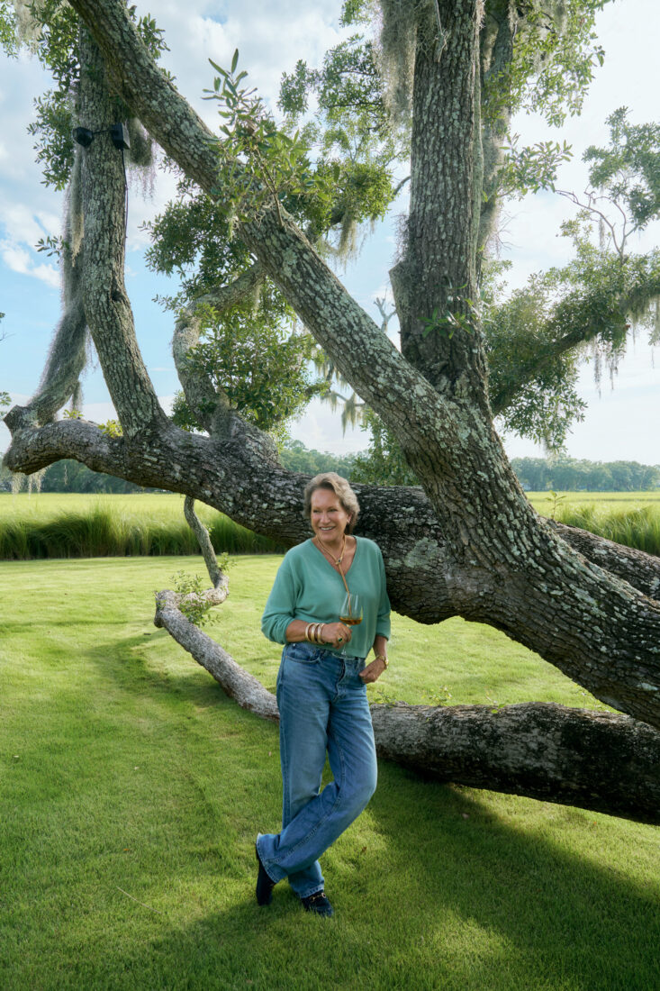 A portrait of a woman holding a glass of wine. She leans against an oak tree