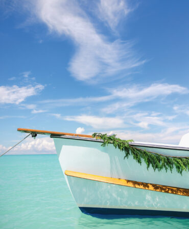 A bow of a boat is decorated with a garland of evergreens. It sits on top of aqua blue water