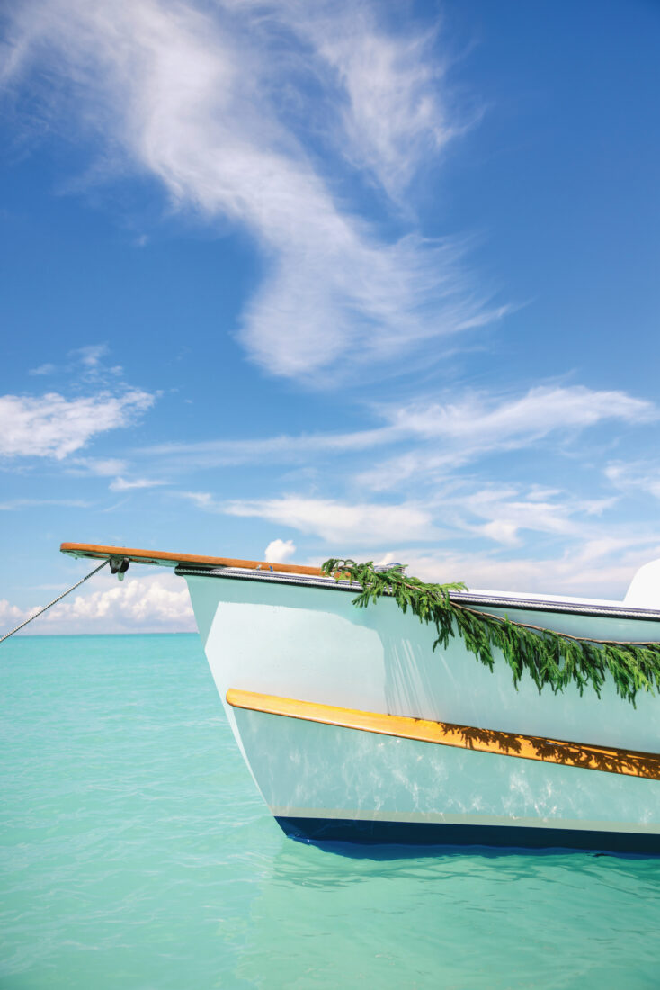 A bow of a boat is decorated with a garland of evergreens. It sits on top of aqua blue water