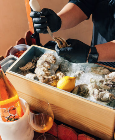 A pair of hands shucks oysters over ice