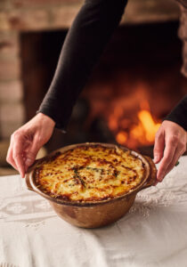 A pair of hands sets down a bowl of turnip gratin on a table