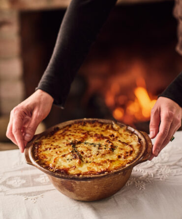 A pair of hands sets down a bowl of turnip gratin on a table