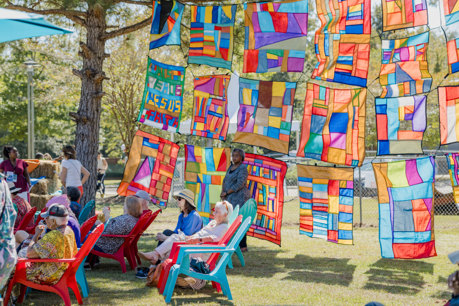 Rows of pieced together colorful quilts hang above seated people