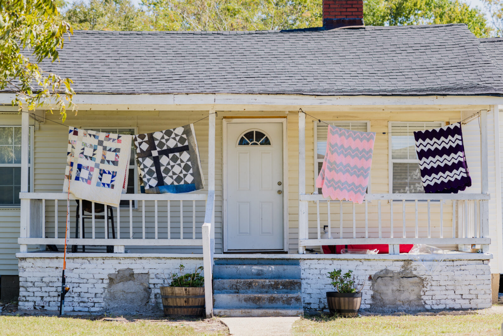 Quilts hang on a laundry line in front of a house