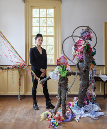 A woman stands in a room with a sculpture of a woman and child and colorful tissue paper