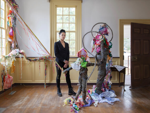 A woman stands in a room with a sculpture of a woman and child and colorful tissue paper