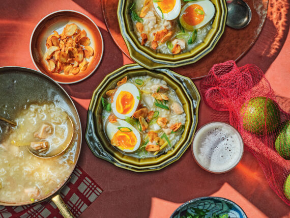 A spread of chicken porridge topped with eggs and bowls of garnishes