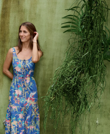 A woman in a blue tropical dress stands against a green background