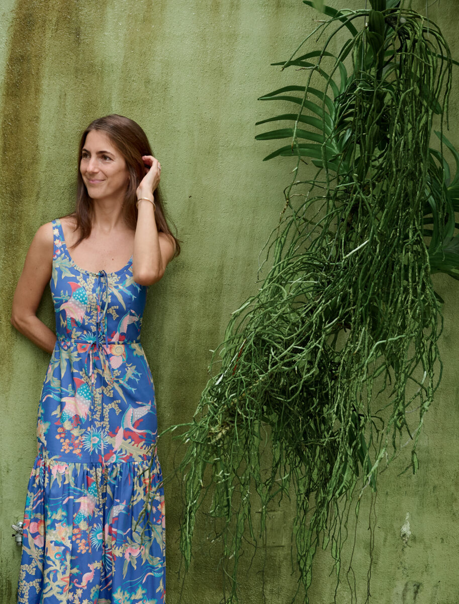 A woman in a blue tropical dress stands against a green background