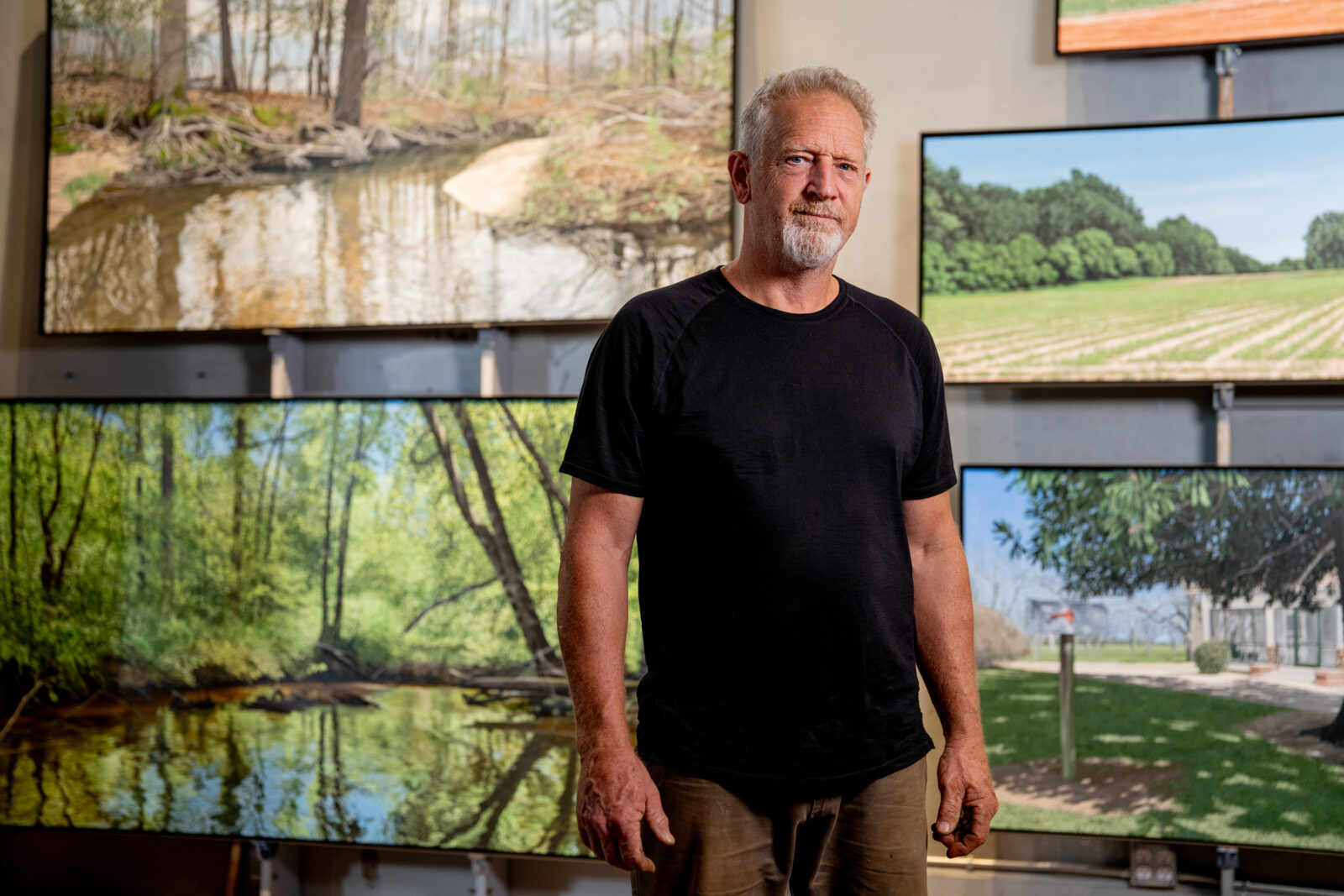 A man stands in front of landscape paintings