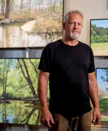 A man stands in front of landscape paintings