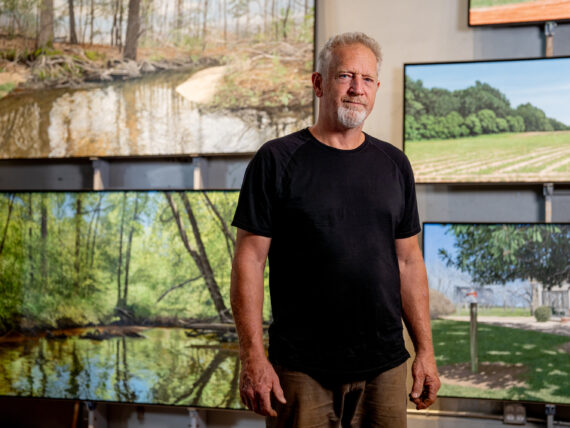 A man stands in front of landscape paintings